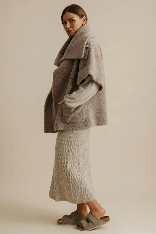 Woman wearing a gray coat and white dress against a beige background