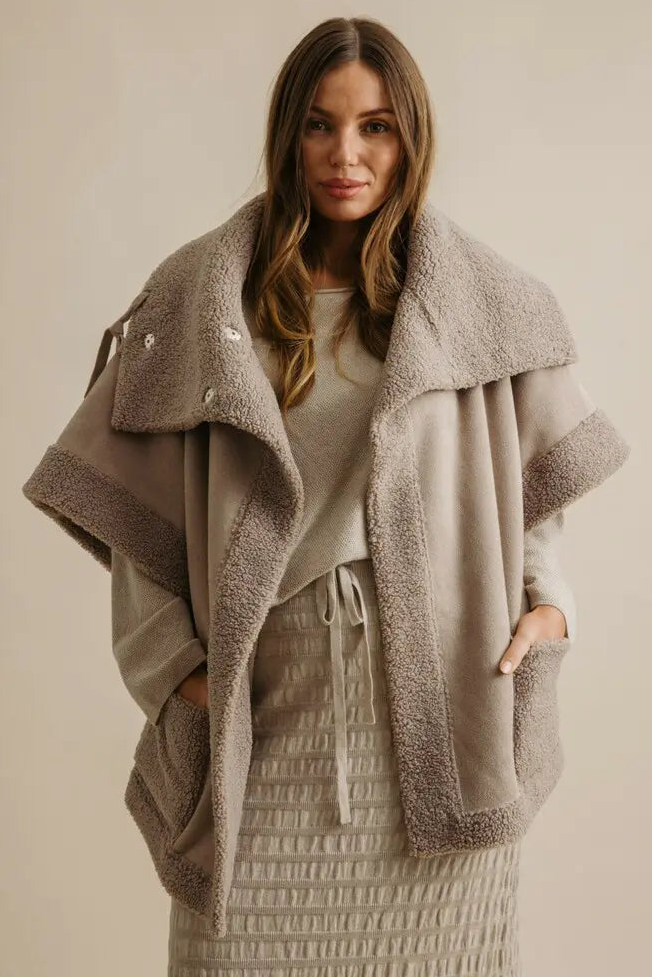 Woman wearing a gray fleece-lined coat against a beige background