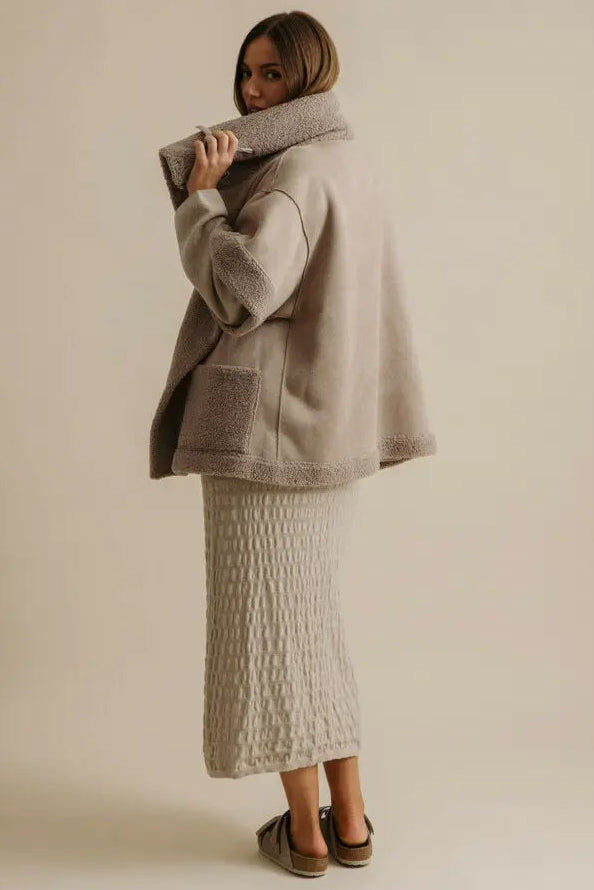 Woman wearing a gray coat and textured skirt against a plain background