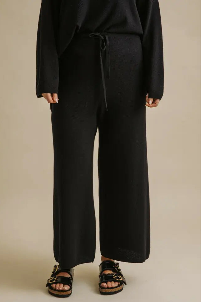 Person wearing black pants and a matching top on a beige background