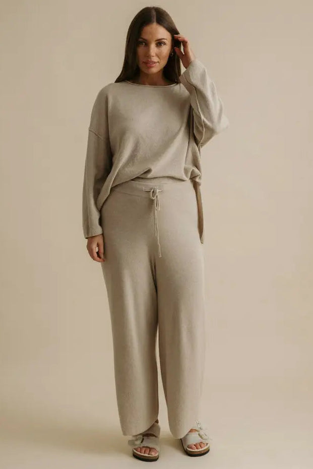 Woman wearing a beige sweater and pants set against a plain background