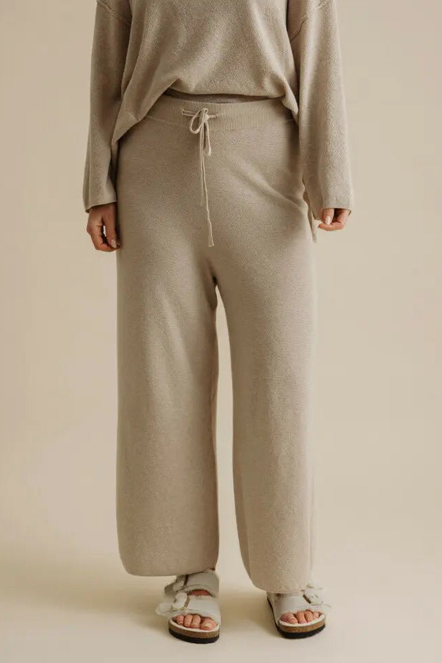 Person wearing beige lounge pants and a matching top on a beige background