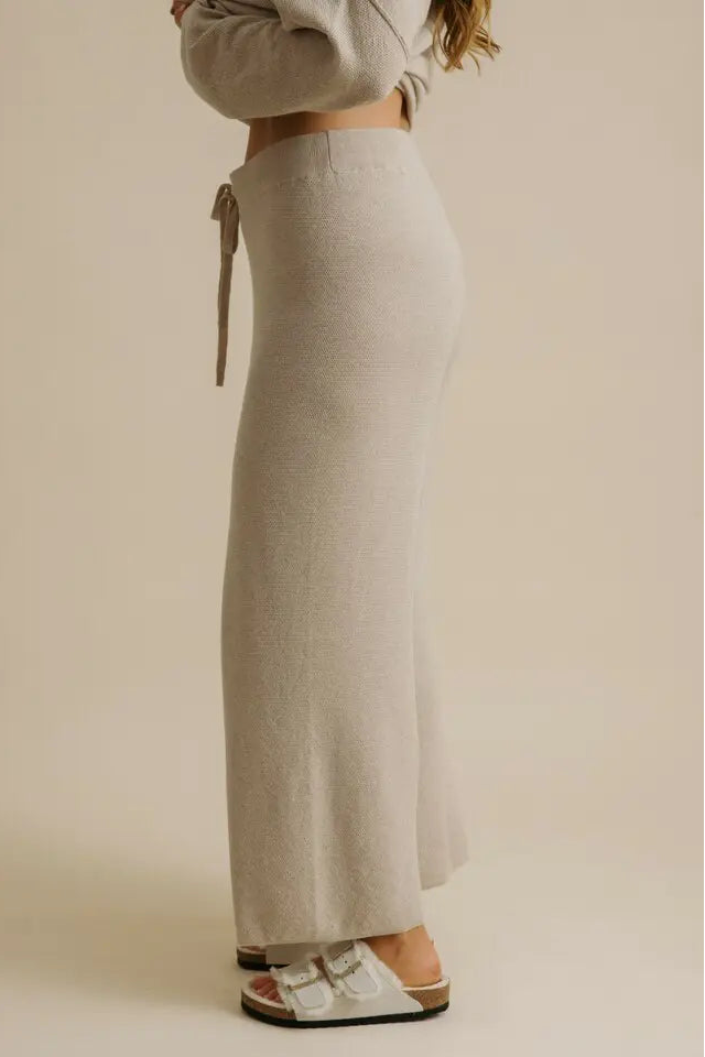 Person wearing a long beige skirt with a plain background