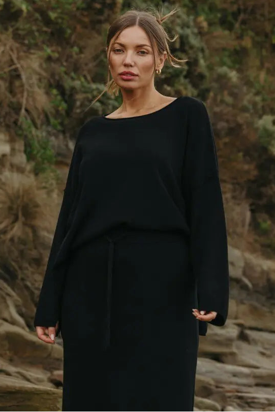 Woman wearing a black outfit standing in a natural setting with greenery.