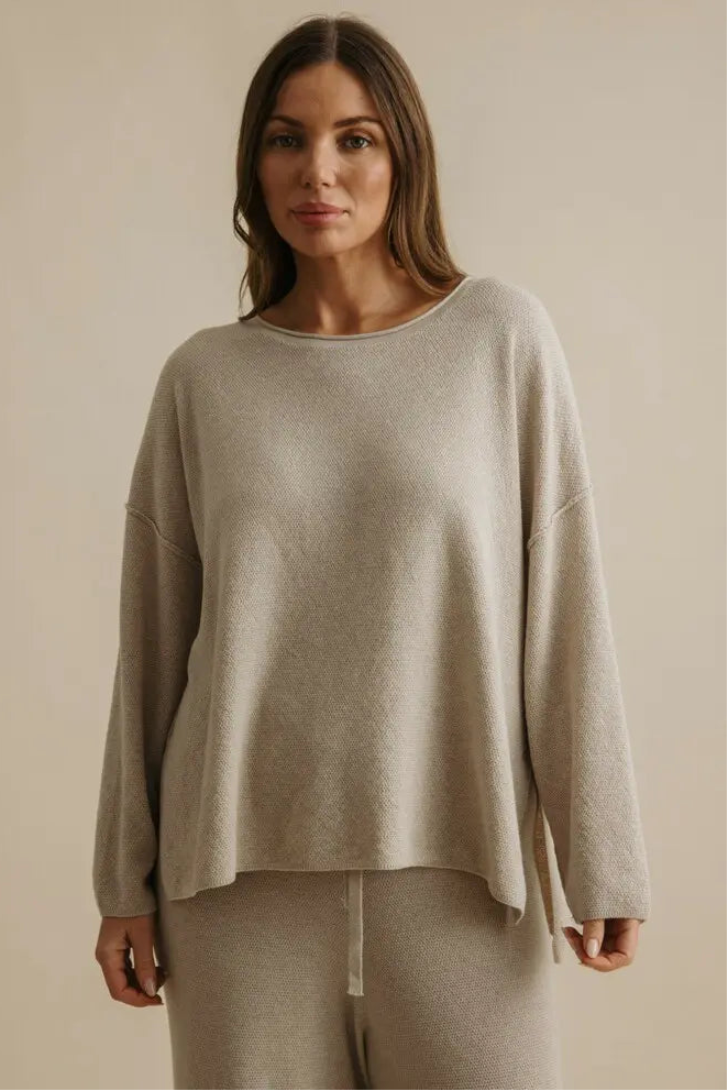 Woman wearing a beige sweater and pants against a beige background
