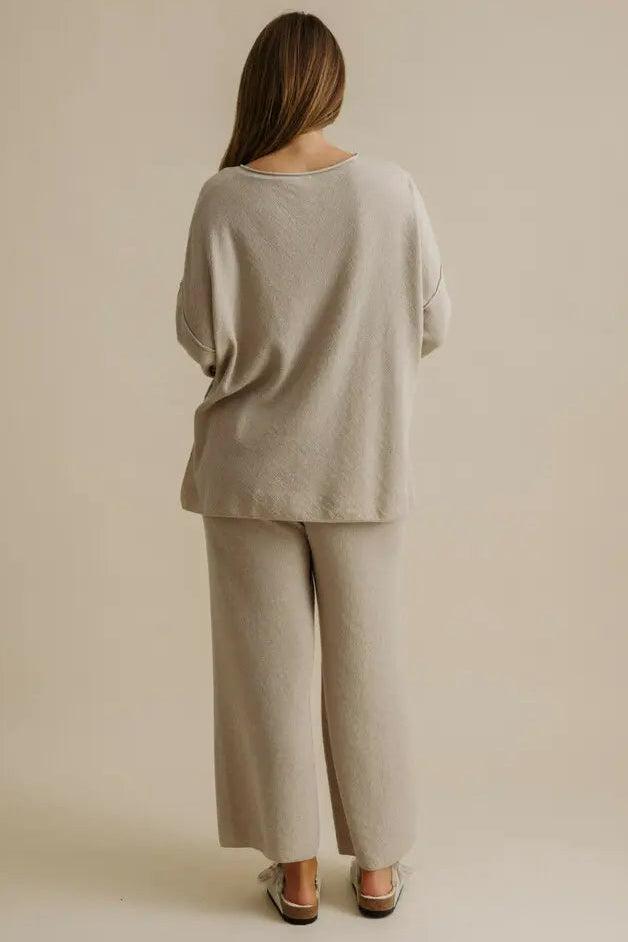 Person wearing a beige outfit standing against a plain background