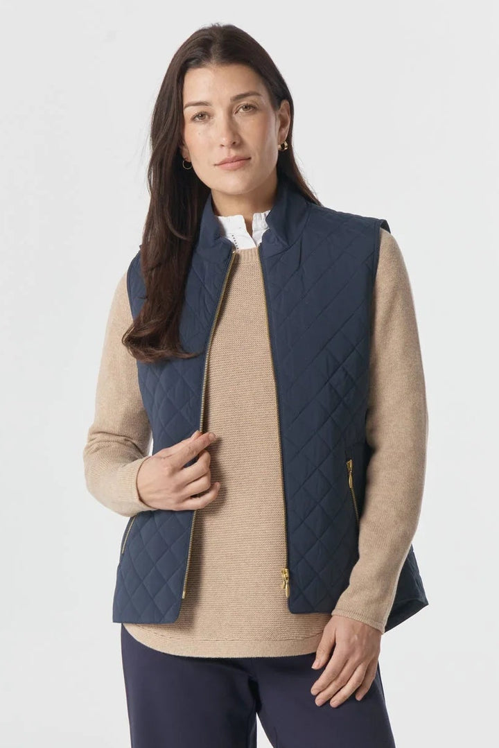 Woman wearing a beige shirt, navy vest, and dark pants on a white background