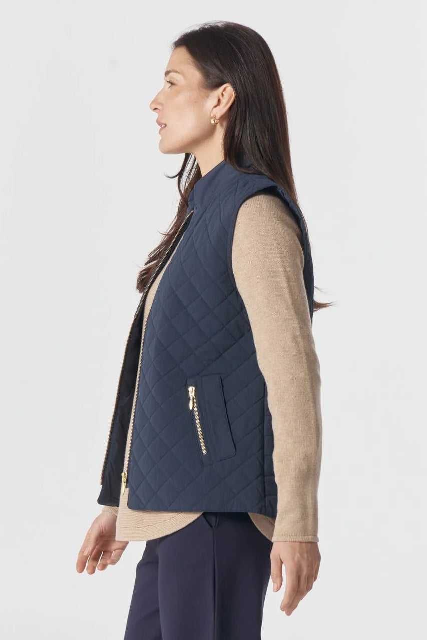 Woman wearing a navy vest over a beige shirt with navy pants on a white background