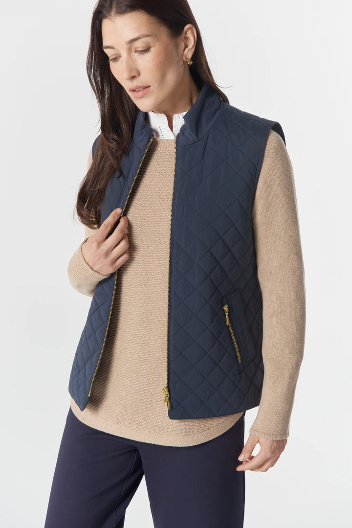 Woman wearing a navy quilted vest over a beige sweater on a white background