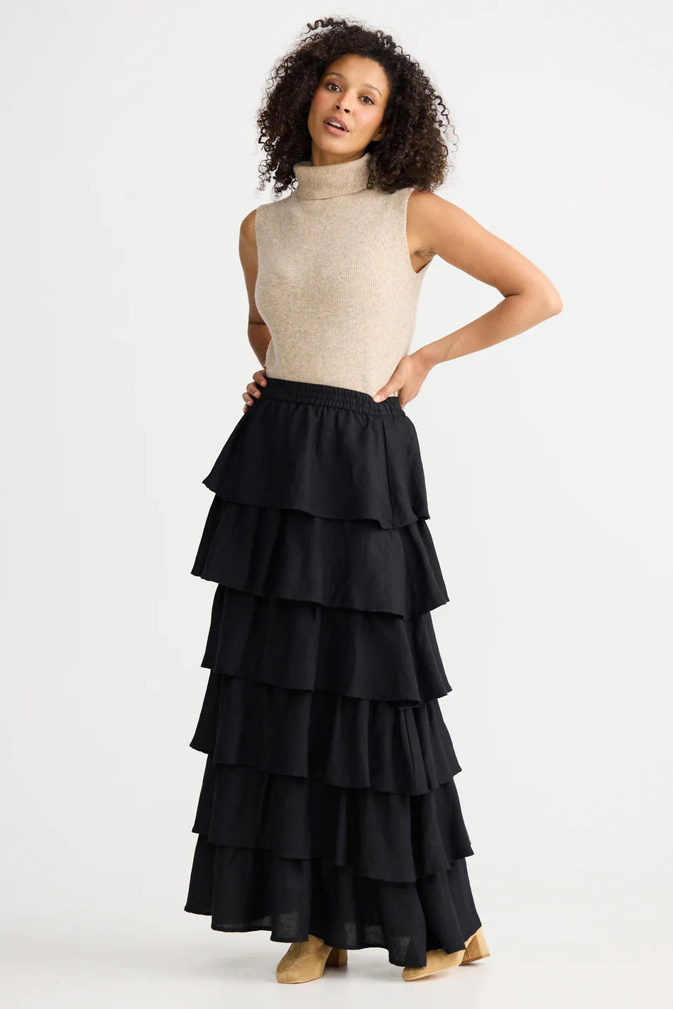 Woman wearing a beige sleeveless top and black tiered skirt on a white background