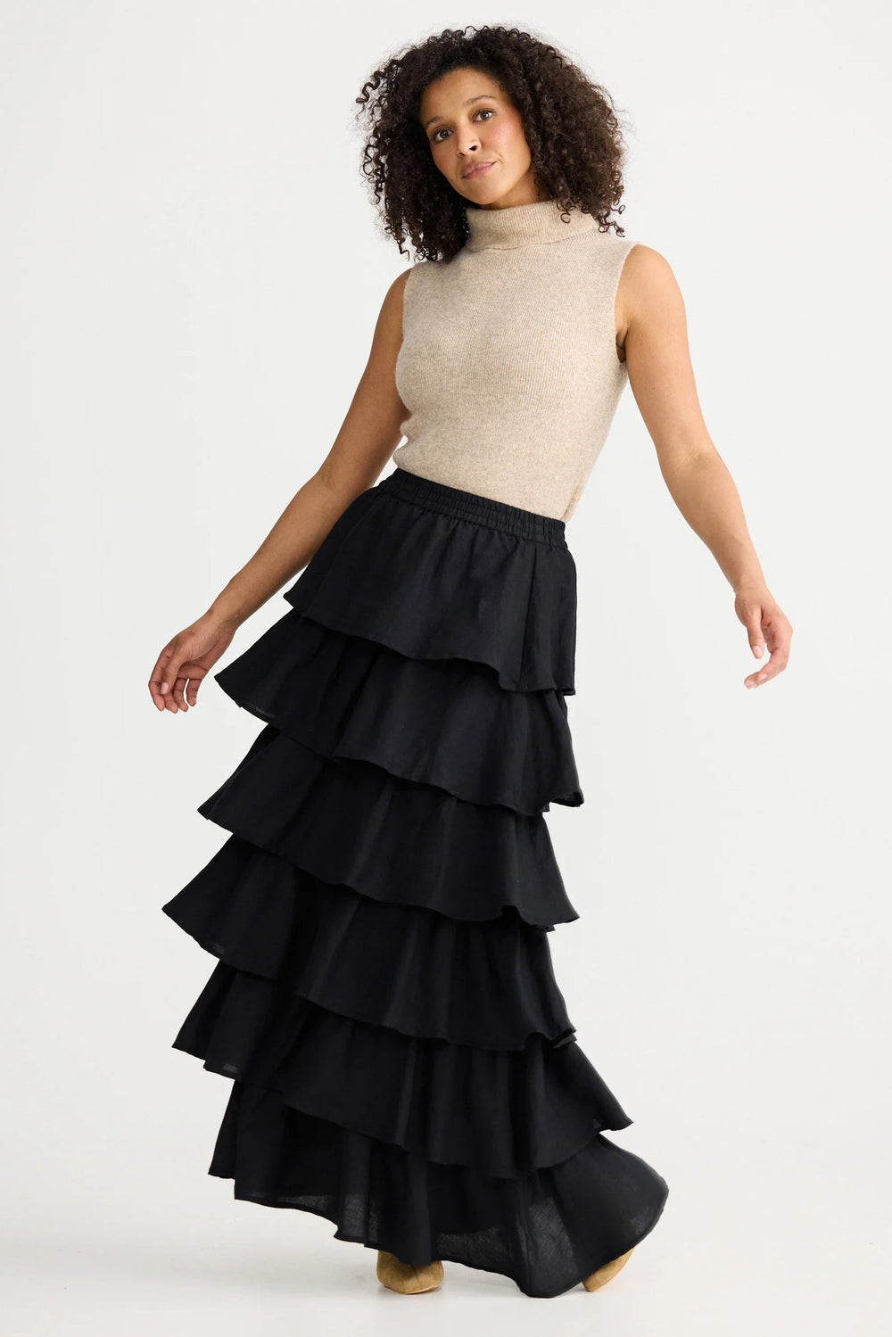 Woman wearing a black tiered skirt and beige top on a white background