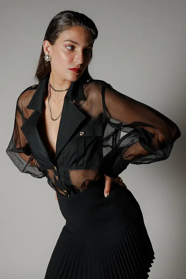 Woman wearing a black outfit with sheer sleeves against a gray background