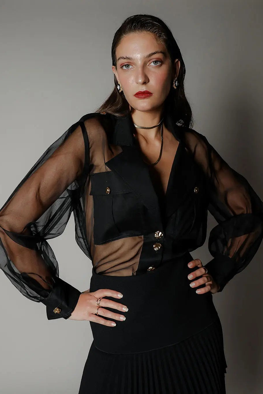 Woman wearing a black outfit with sheer sleeves against a gray background