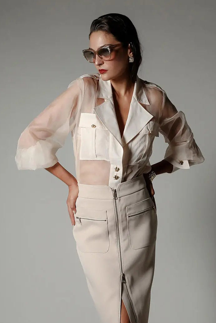 Woman wearing a beige outfit with sheer sleeves against a gray background