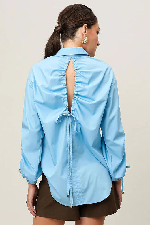 Woman wearing a light blue shirt with a cutout back design on a plain background
