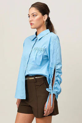 Woman wearing a light blue shirt and brown shorts on a plain background