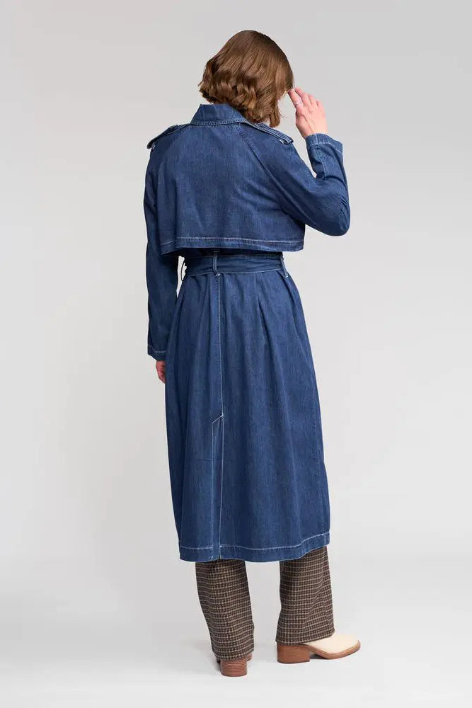 Person wearing a long blue denim coat on a white background