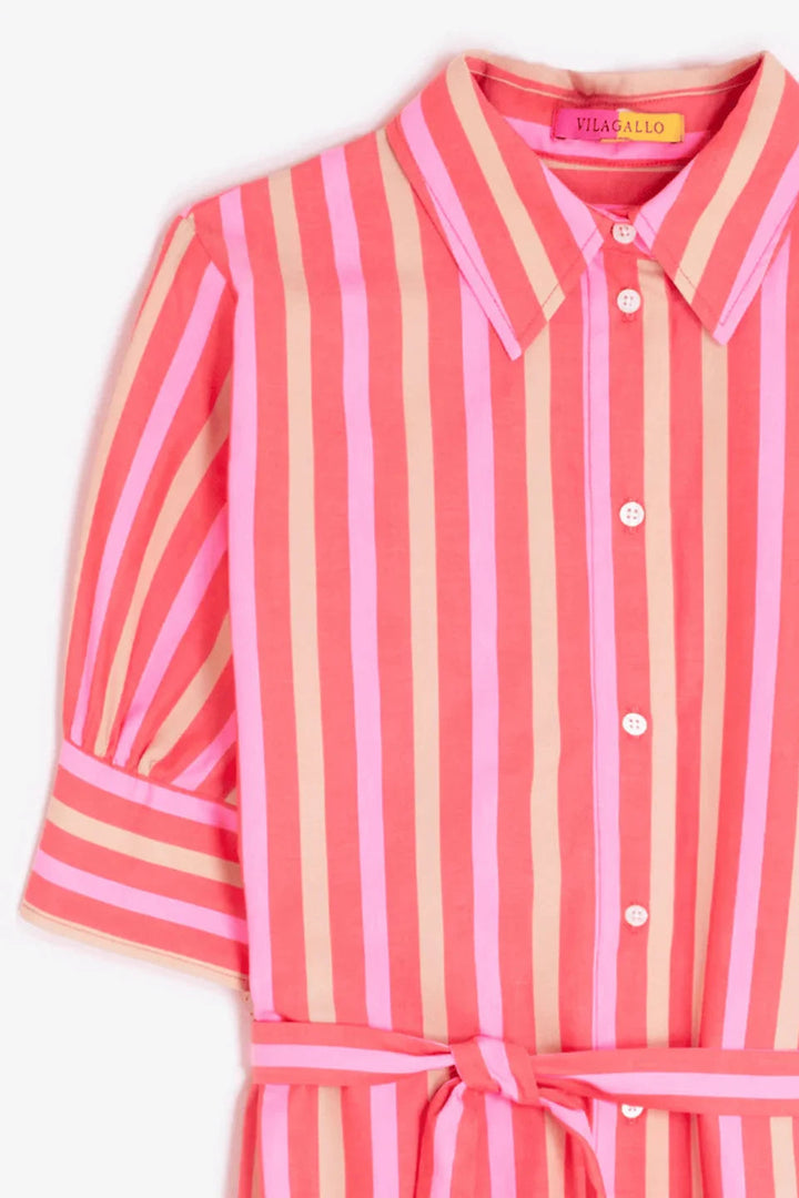 A close-up of a collared button-front shirt dress with vertical pink, coral, and peach stripes, featuring puff sleeves and a matching tie belt at the waist. A yellow brand label reading 'VILAI ALLO' is visible inside the collar.