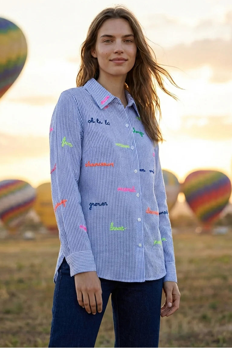 Woman wearing a blue shirt with colorful text design in front of hot air balloons.