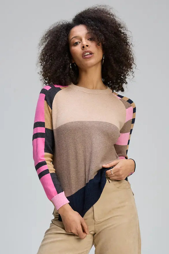 Woman wearing a colorful long-sleeve top and beige pants on a plain background