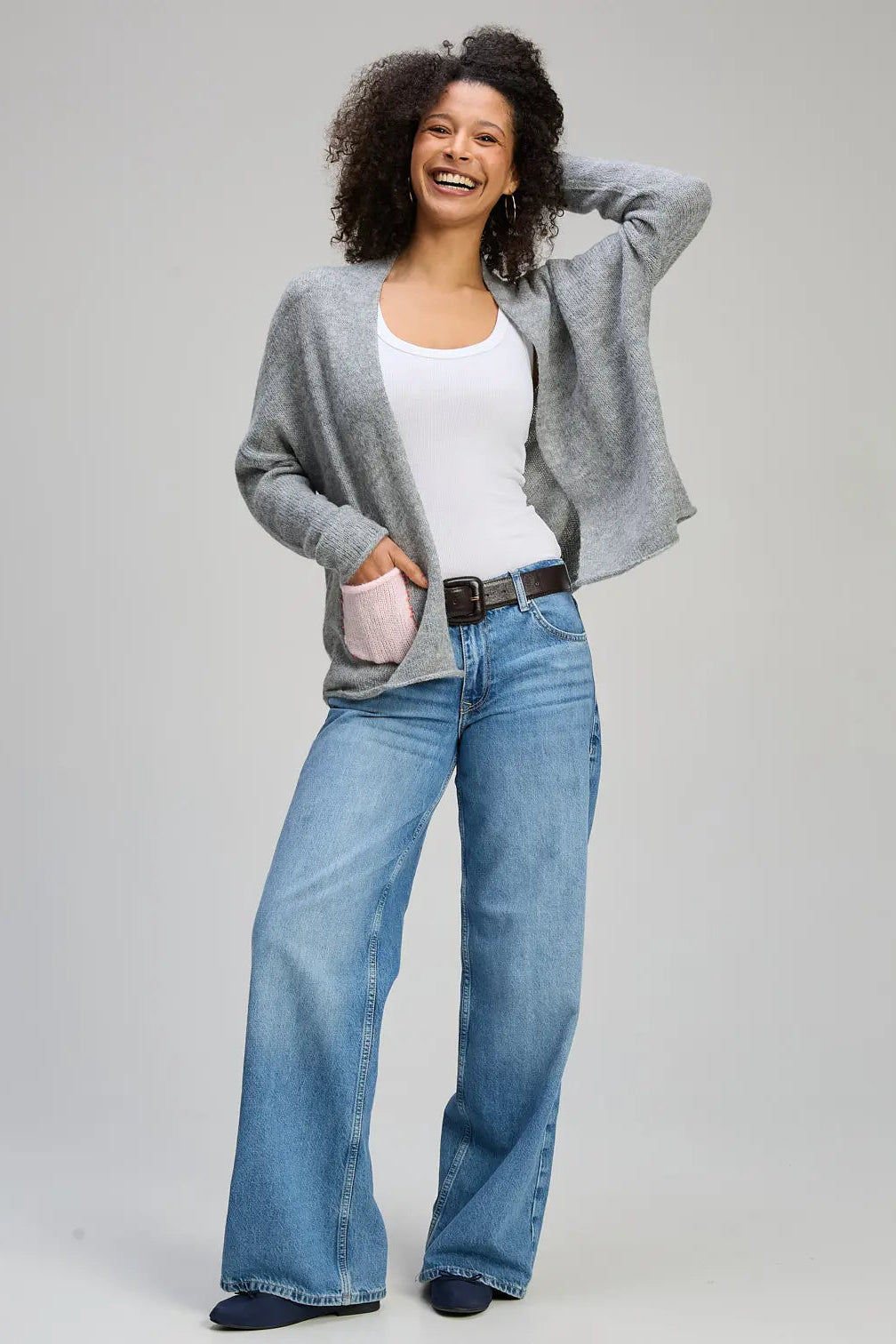 Woman wearing a gray cardigan, white top, and blue jeans on a light gray background
