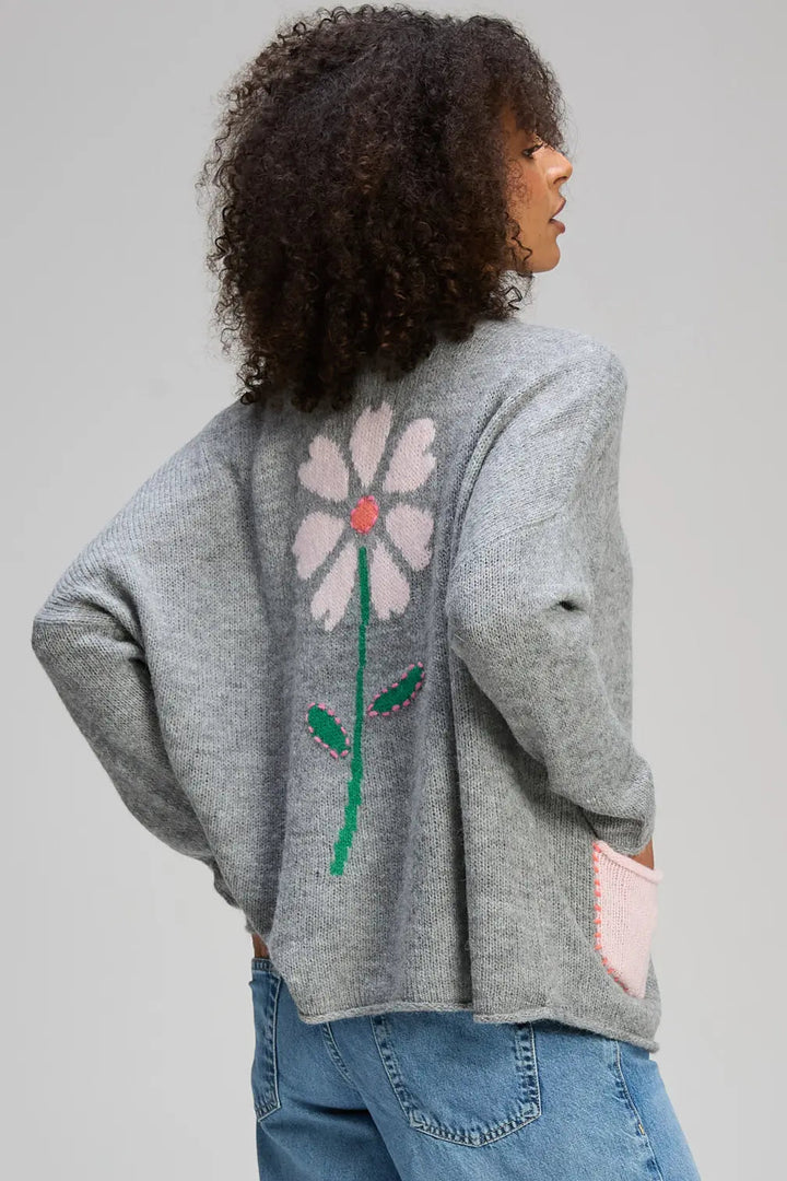 Person wearing a gray sweater with a flower design on the back against a plain background