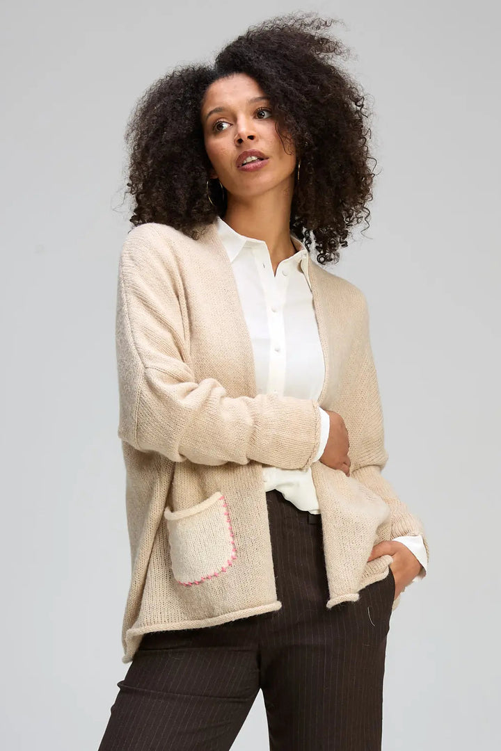 Woman wearing a beige cardigan over a white shirt with a gray background
