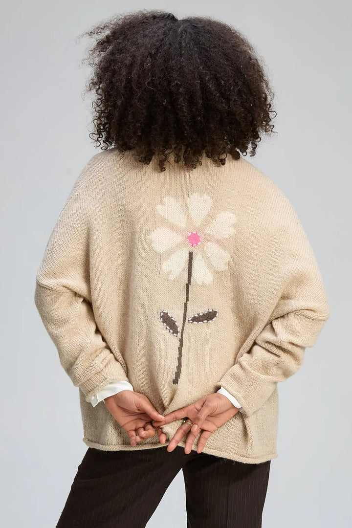 Person wearing a beige sweater with a floral design on the back against a gray background