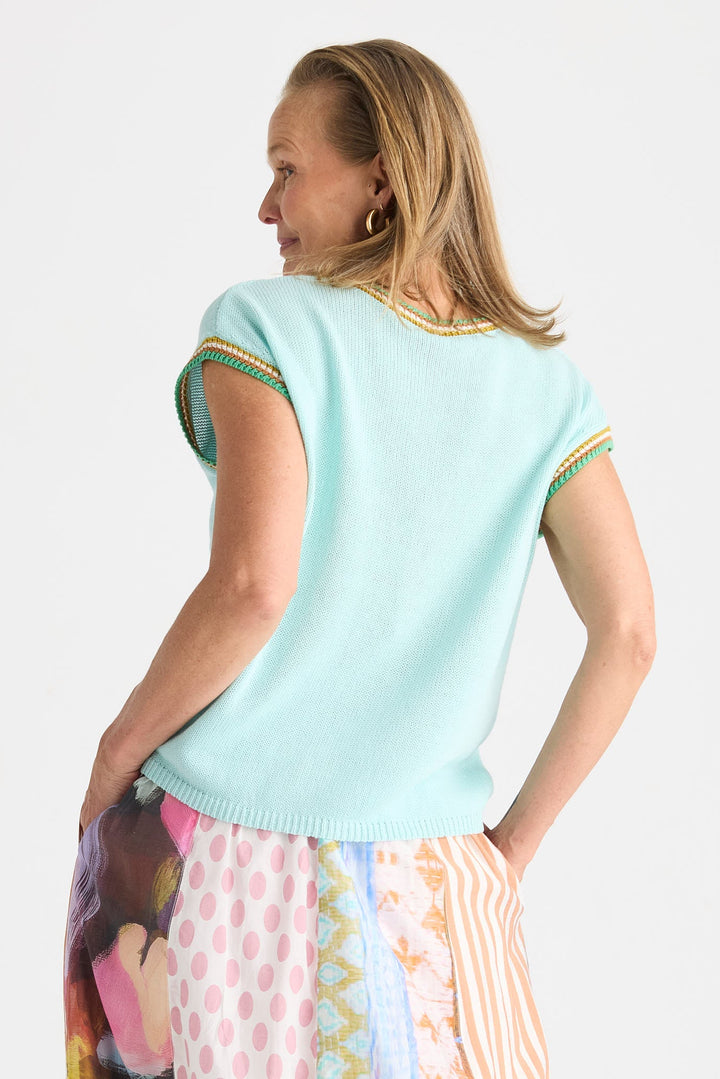 A woman shown from the back wearing a light mint green short-sleeve knit top with yellow and green striped trim on the sleeve cuffs, paired with a colorful patterned skirt, against a plain light gray background.