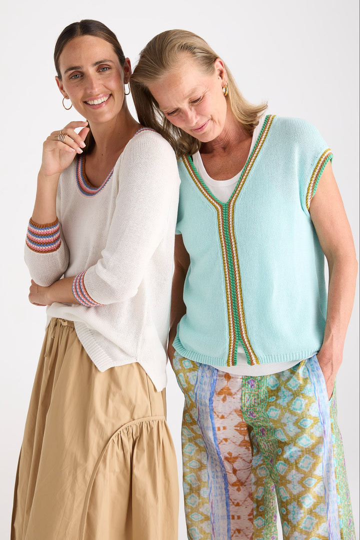 Two women modeling knit apparel against a plain light background. The woman on the left wears a cream long-sleeve top with striped trim and a beige skirt.
