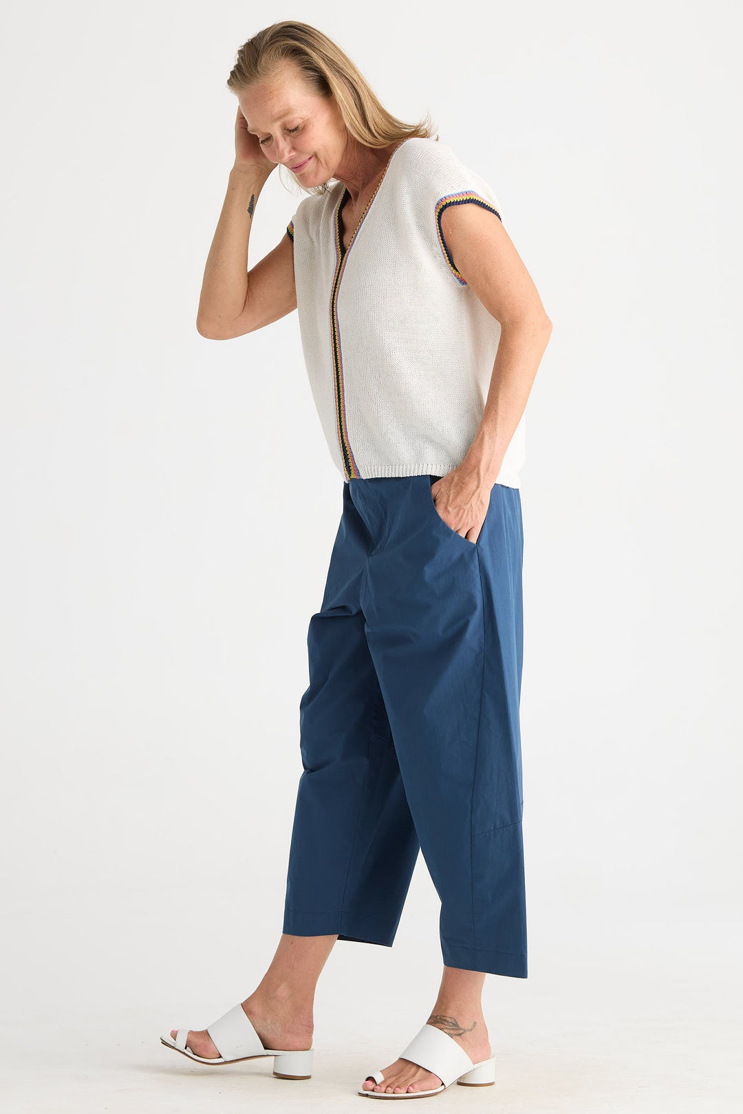 A woman modeling a pair of wide-leg cropped pants in navy blue, paired with a white knit top and white slide sandals, against a plain white studio background.