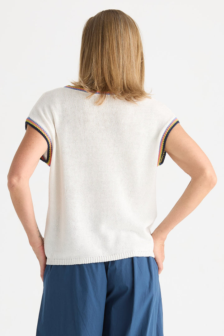 A woman shown from the back wearing a short-sleeve knit top in off-white with striped trim at the sleeve cuffs, paired with blue pants, against a plain light background.