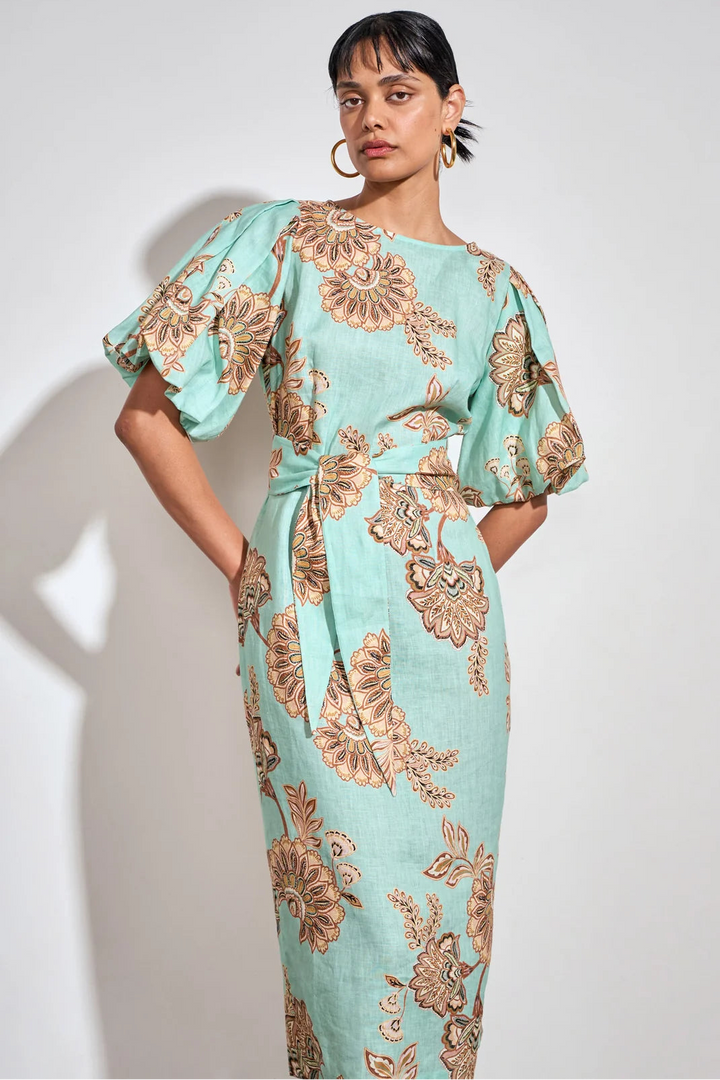 A woman modeling a mint green midi dress with a brown floral pattern, featuring voluminous puff sleeves and a matching waist tie, set against a plain light gray background.