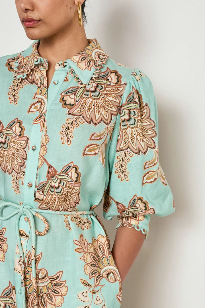 A close-up of a model wearing a mint green shirt dress with a brown and beige floral paisley pattern, featuring puff sleeves and a tie waist.