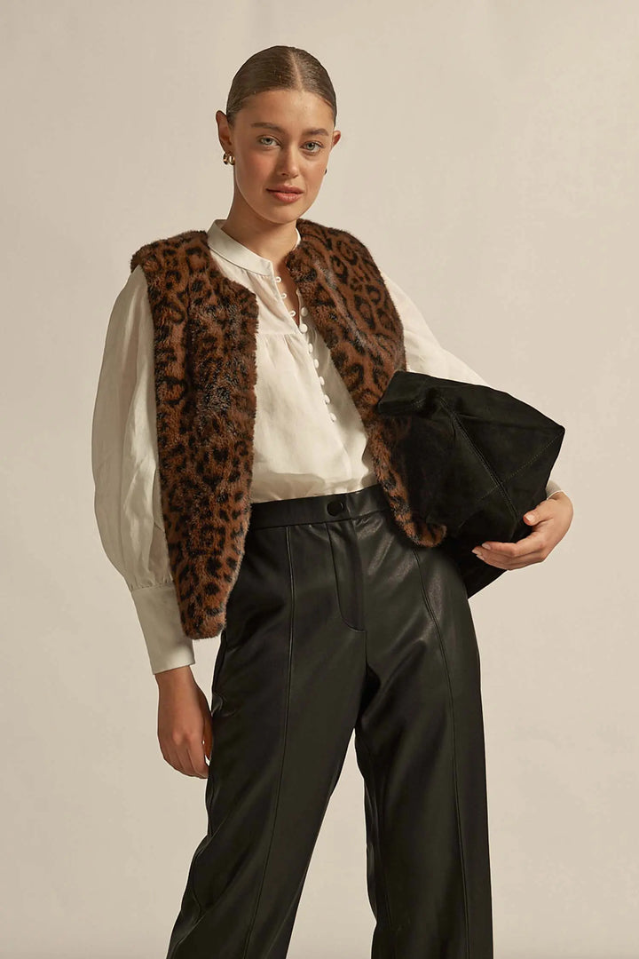 Person wearing a leopard print vest over a white shirt with black pants, holding a black clutch.