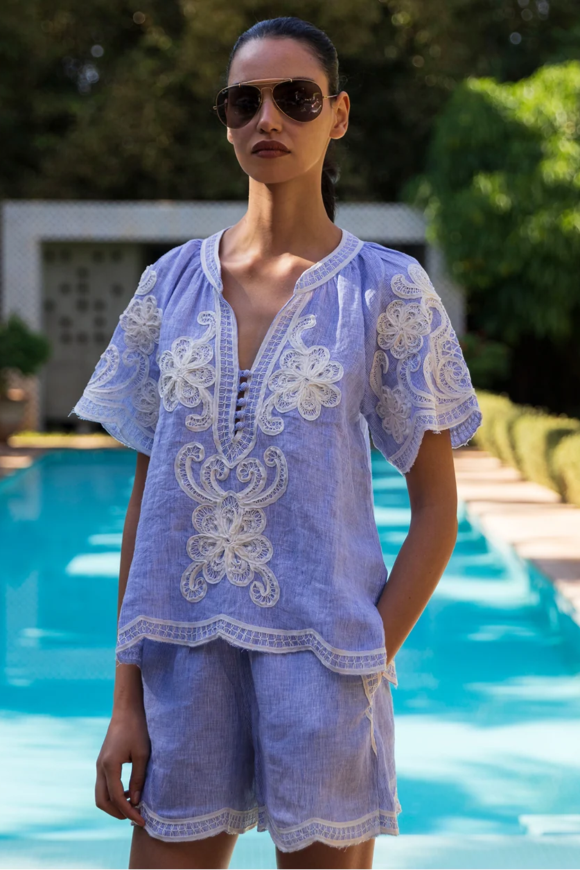 Woman wearing a light blue embroidered outfit by a pool