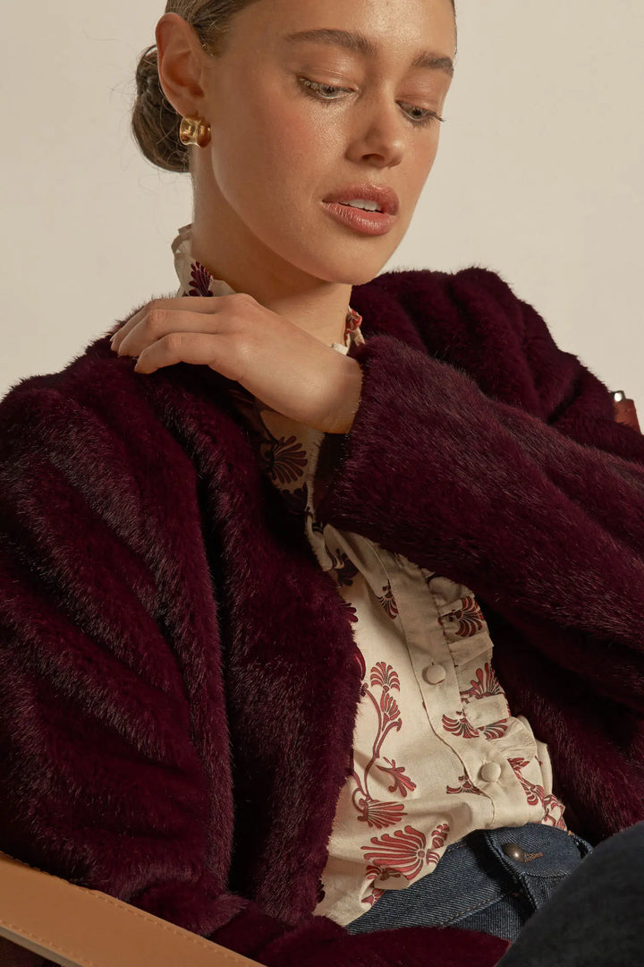 Woman wearing a burgundy fur coat over a patterned shirt with a neutral background