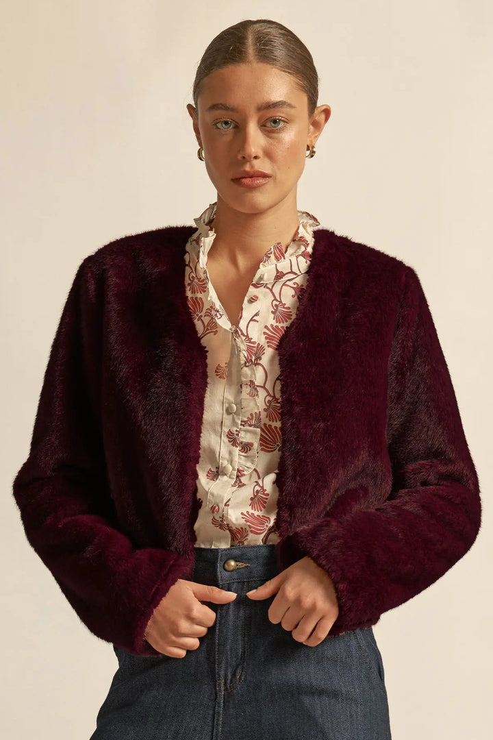 Woman wearing a burgundy cardigan over a floral blouse with dark jeans on a beige background