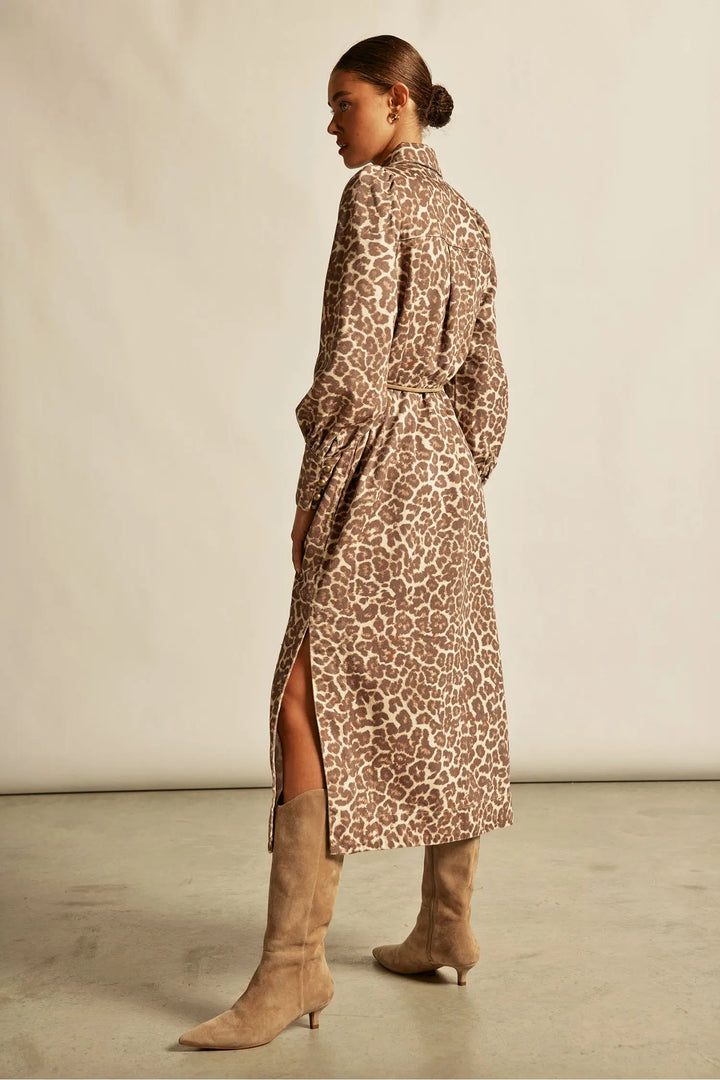 Woman wearing a leopard print dress with a high slit and matching boots on a plain background