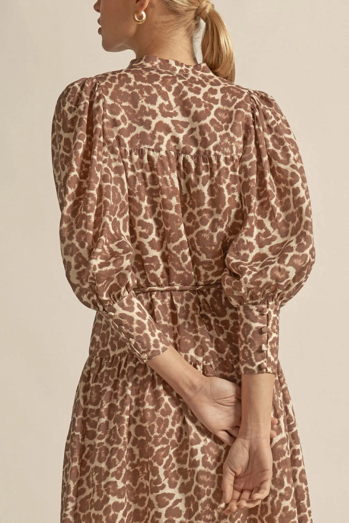 Person wearing a leopard print dress with long sleeves on a beige background