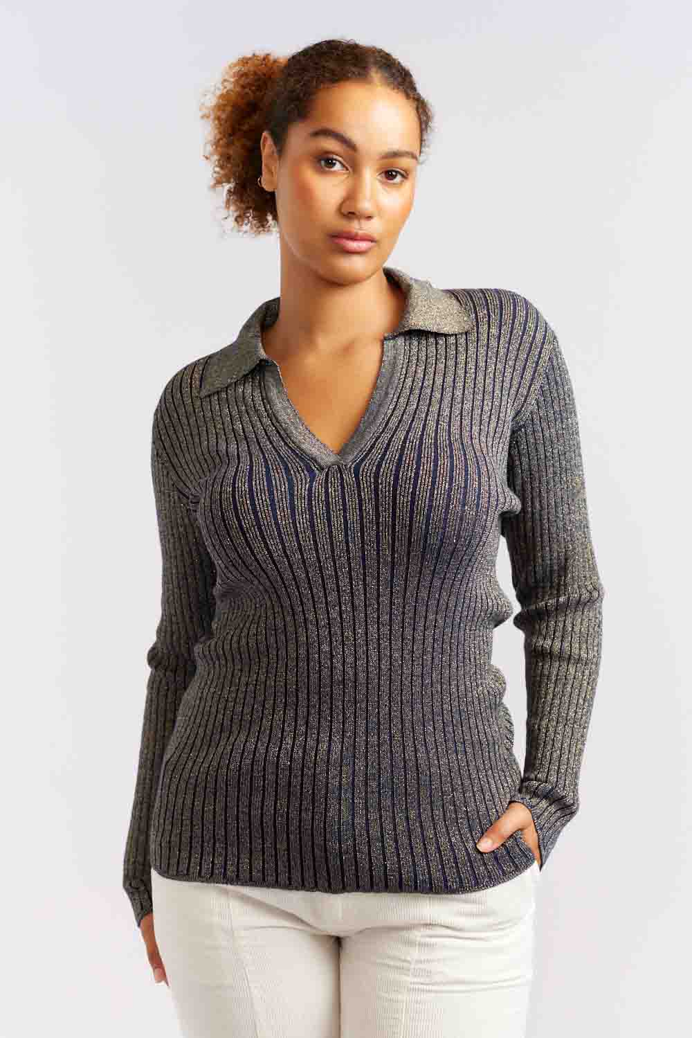 A woman wearing a navy ribbed knit long-sleeve top with a v-neck collar, paired with white pants.