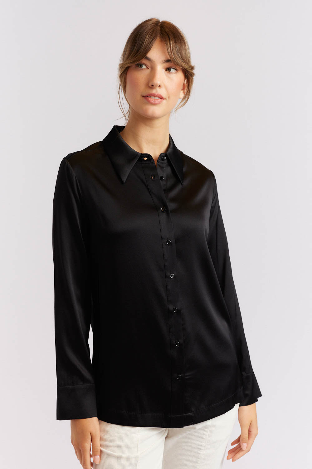 A woman wearing a black silk shirt with long sleeves, button-up front, and a collar.